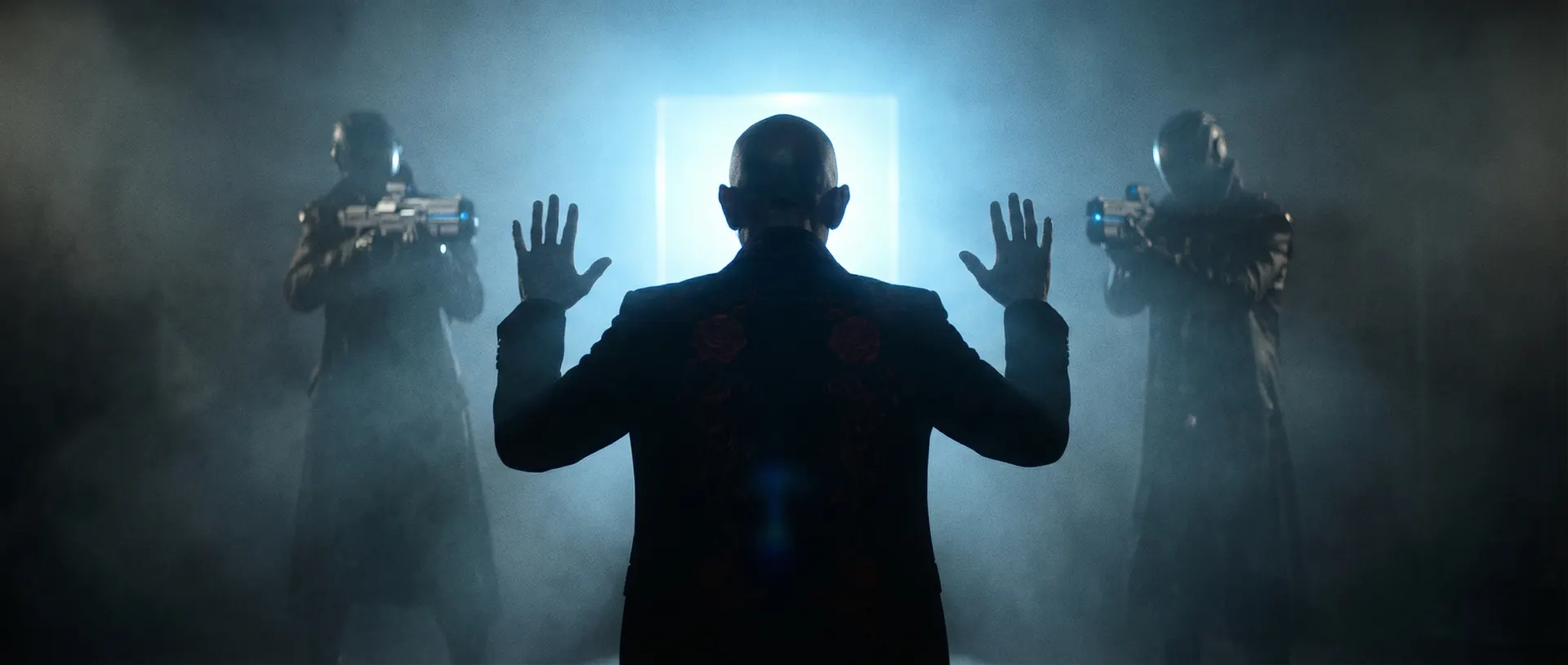 A bald man raises his hands in surrender between two armed guards in a fog-filled room.